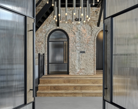 Zwarte stalen deuren met geribbeld glas en een boogvorm, gecombineerd met een rustieke bakstenen muur en moderne verlichting.