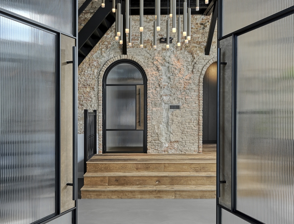 Zwarte stalen deuren met geribbeld glas en een boogvorm, gecombineerd met een rustieke bakstenen muur en moderne verlichting.