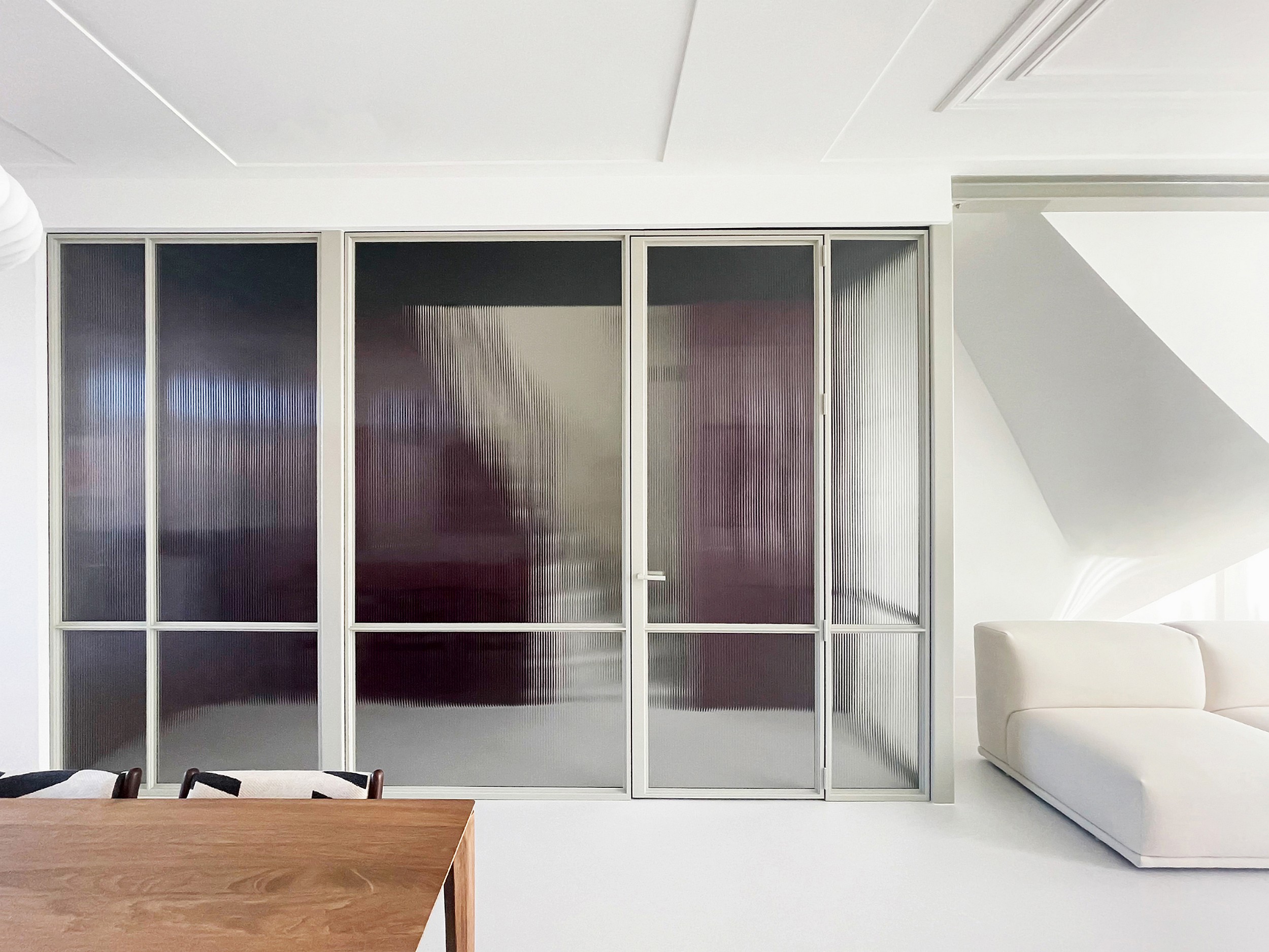 Witte stalen deur met geribbeld glas als stijlvolle roomdivider in een modern interieur.
