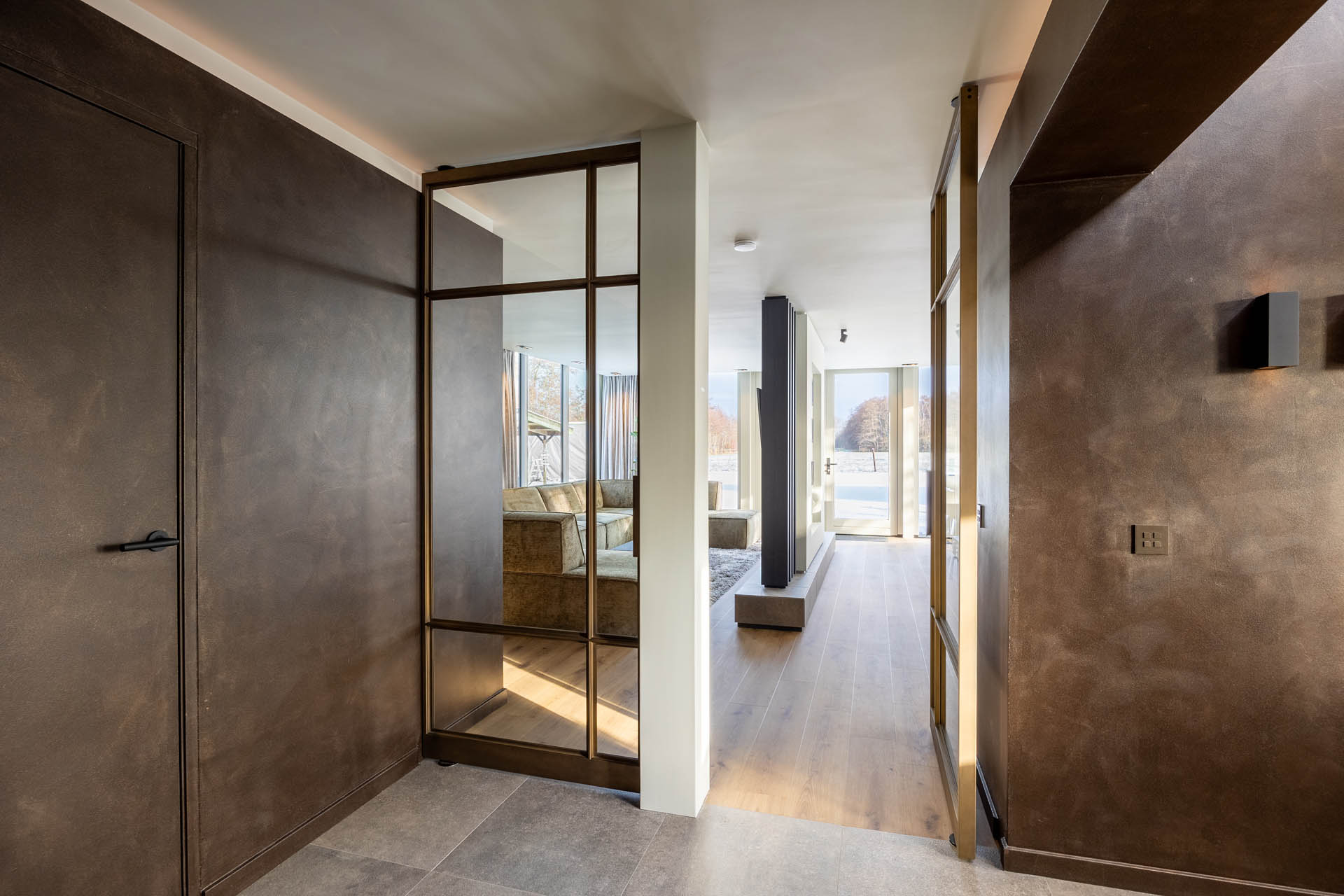 Messing stalen taatsdeur met glas in modern interieur met warme tinten en natuurlijke lichtinval.