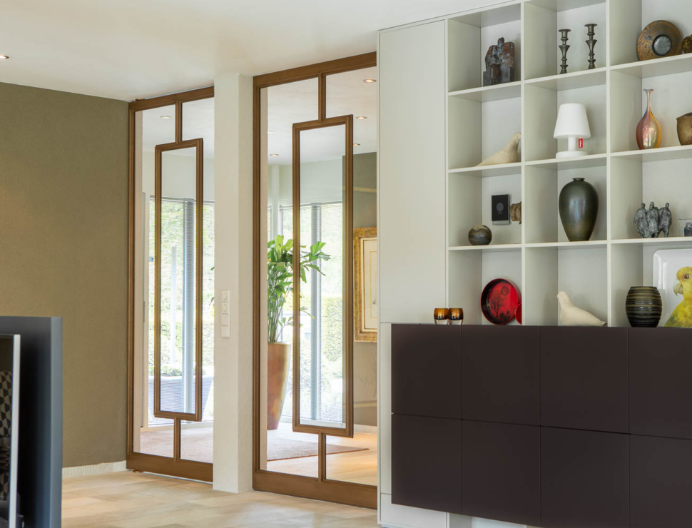 Dubbele bronzen stalen deuren met glas als elegante scheiding tussen hal en woonkamer.