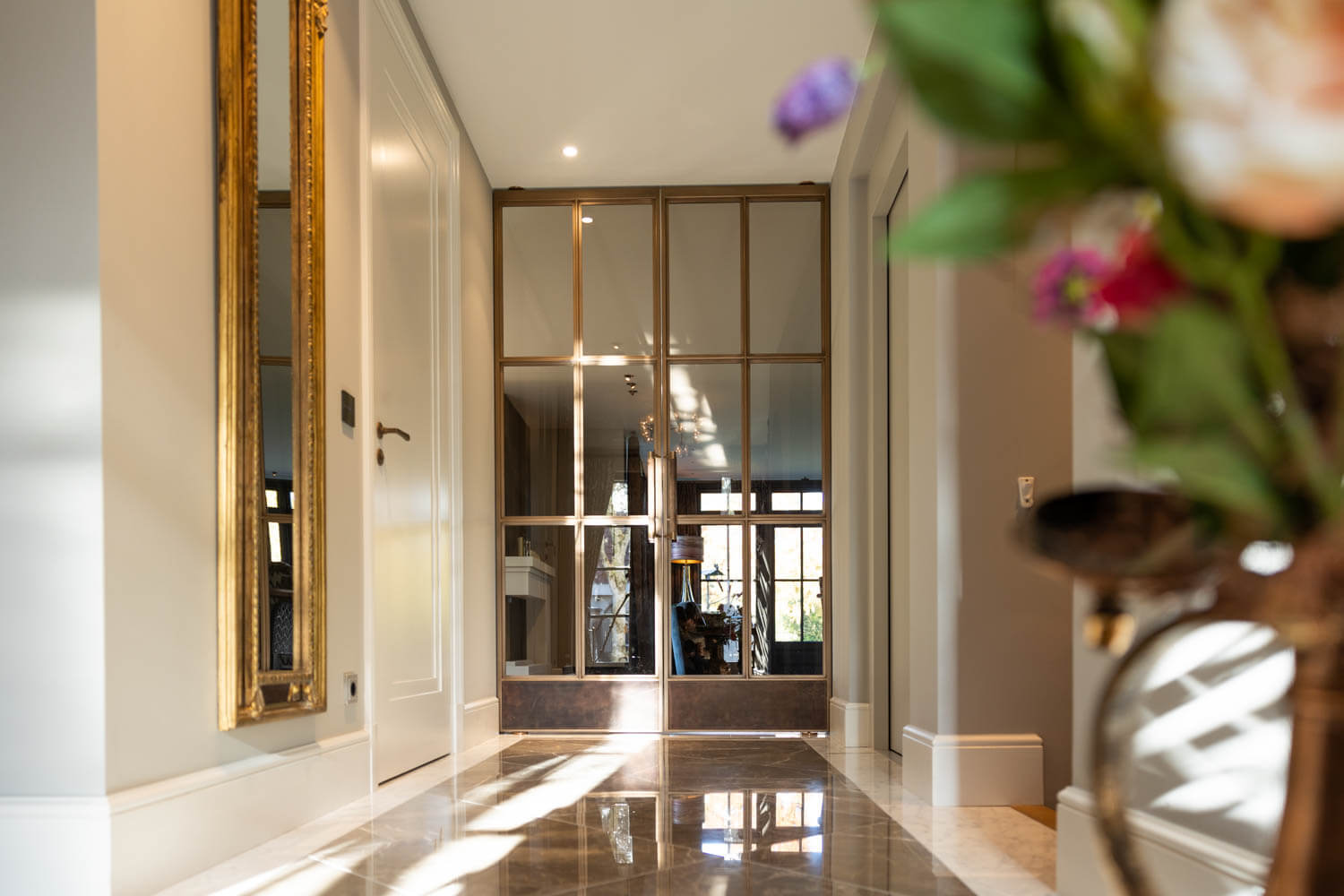 Luxe hal met bronzen stalen taatsdeuren en marmeren vloer, weerspiegelend het klassieke interieur.