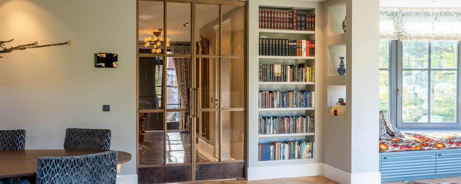 Dubbele bronzen deuren met leren handgrepen als stijlvolle roomdivider bij een boekenkast.