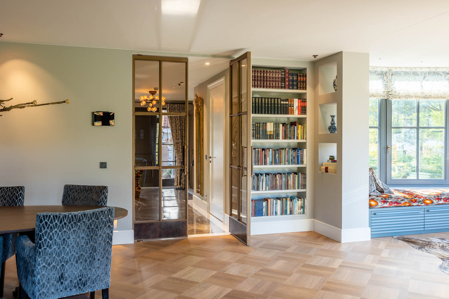 Luxe woonkamer met bronzen taatsdeuren en ingebouwde boekenkast, gecombineerd met warme houten vloeren.