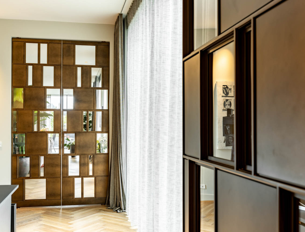 Unieke bronzen stalen deuren in een luxe interieur met visgraatvloer en natuurlijke lichtinval.