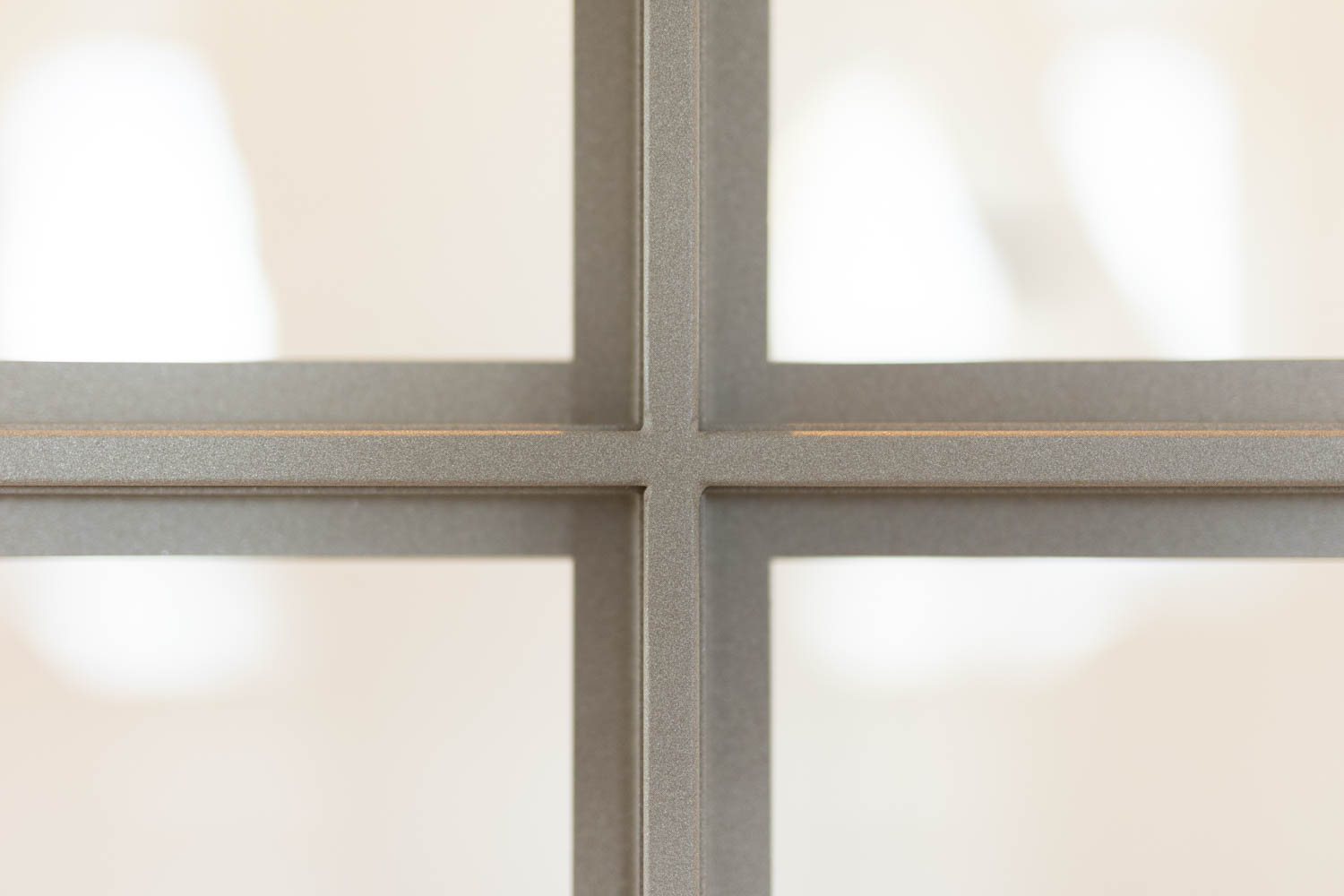 Detail van een beige stalen deur met verfijnde glasverdeling en strakke afwerking.