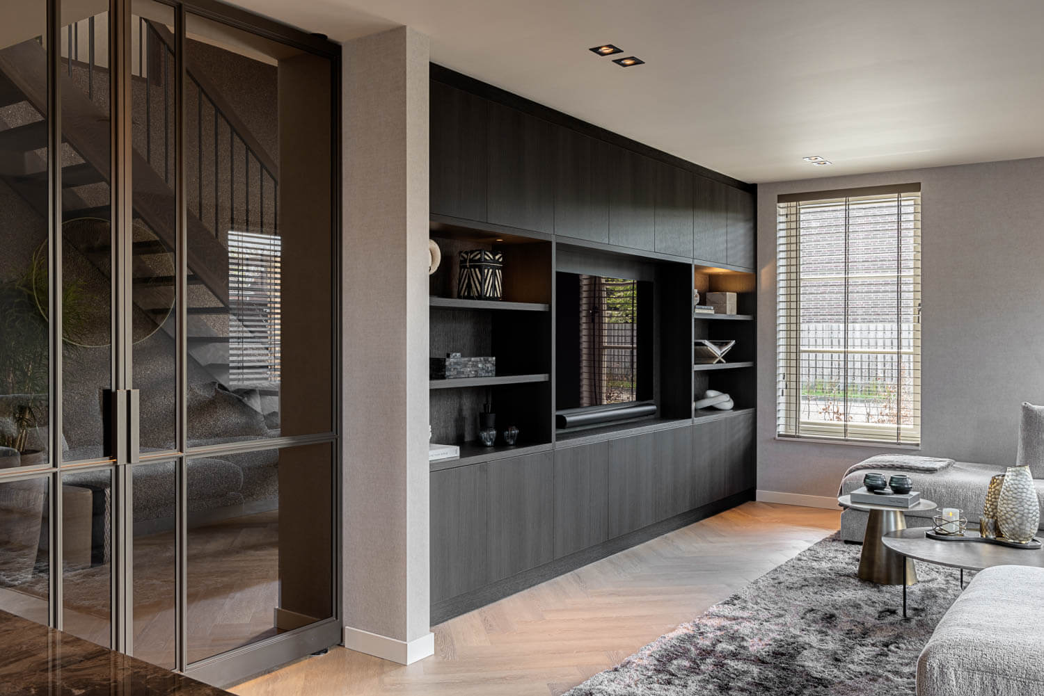 Anodic Brown stalen taatsdeur met glas in modern interieur met visgraatvloer en maatwerk kastenwand.