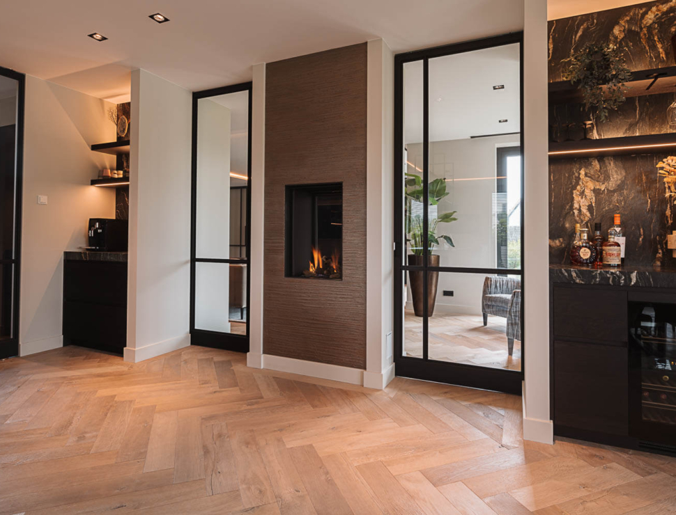 Zwarte stalen taatsdeuren met glas, geplaatst in een modern interieur met visgraatvloer en ingebouwde haard.