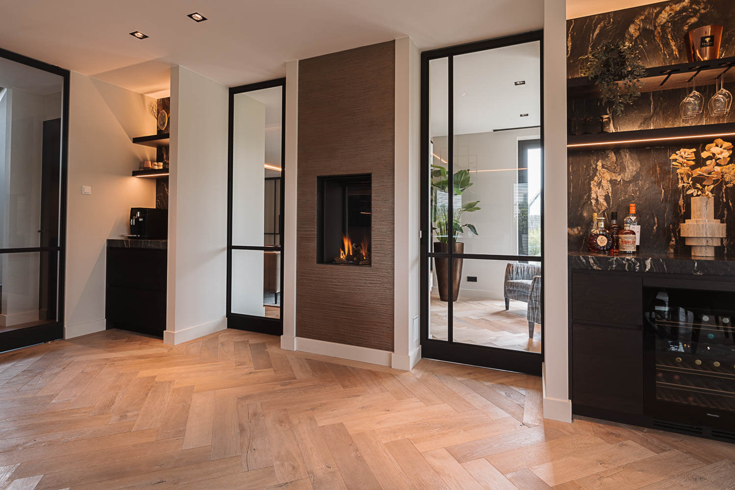 Zwarte stalen taatsdeuren met glas, geplaatst in een modern interieur met visgraatvloer en ingebouwde haard.