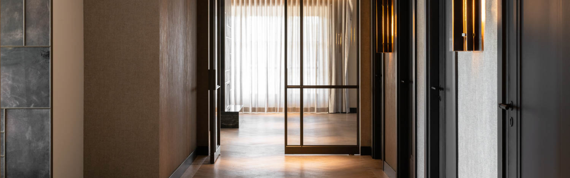 Luxe zwarte stalen taatsdeur met glas in moderne hal met visgraatvloer en warme verlichting.