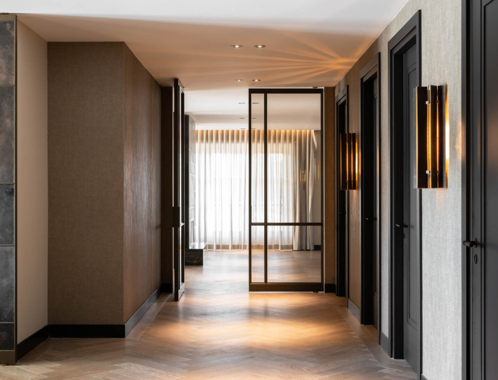 Luxe zwarte stalen taatsdeur met glas in moderne hal met visgraatvloer en warme verlichting.