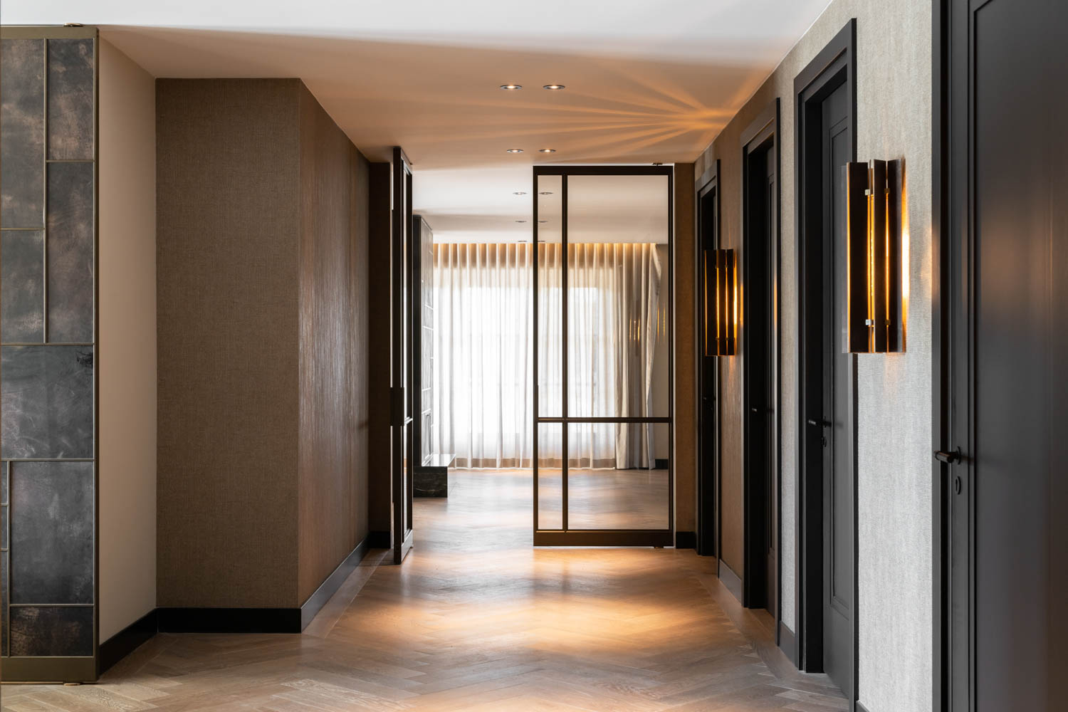 Luxe zwarte stalen taatsdeur met glas in moderne hal met visgraatvloer en warme verlichting.