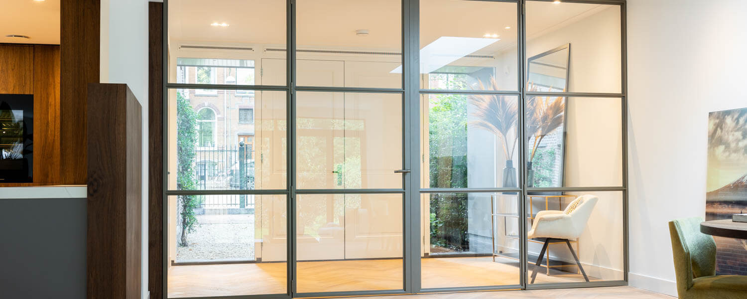 Luxe stalen schuifdeuren met kozijn in een modern interieur met visgraatvloer, creëert een open en lichte sfeer.