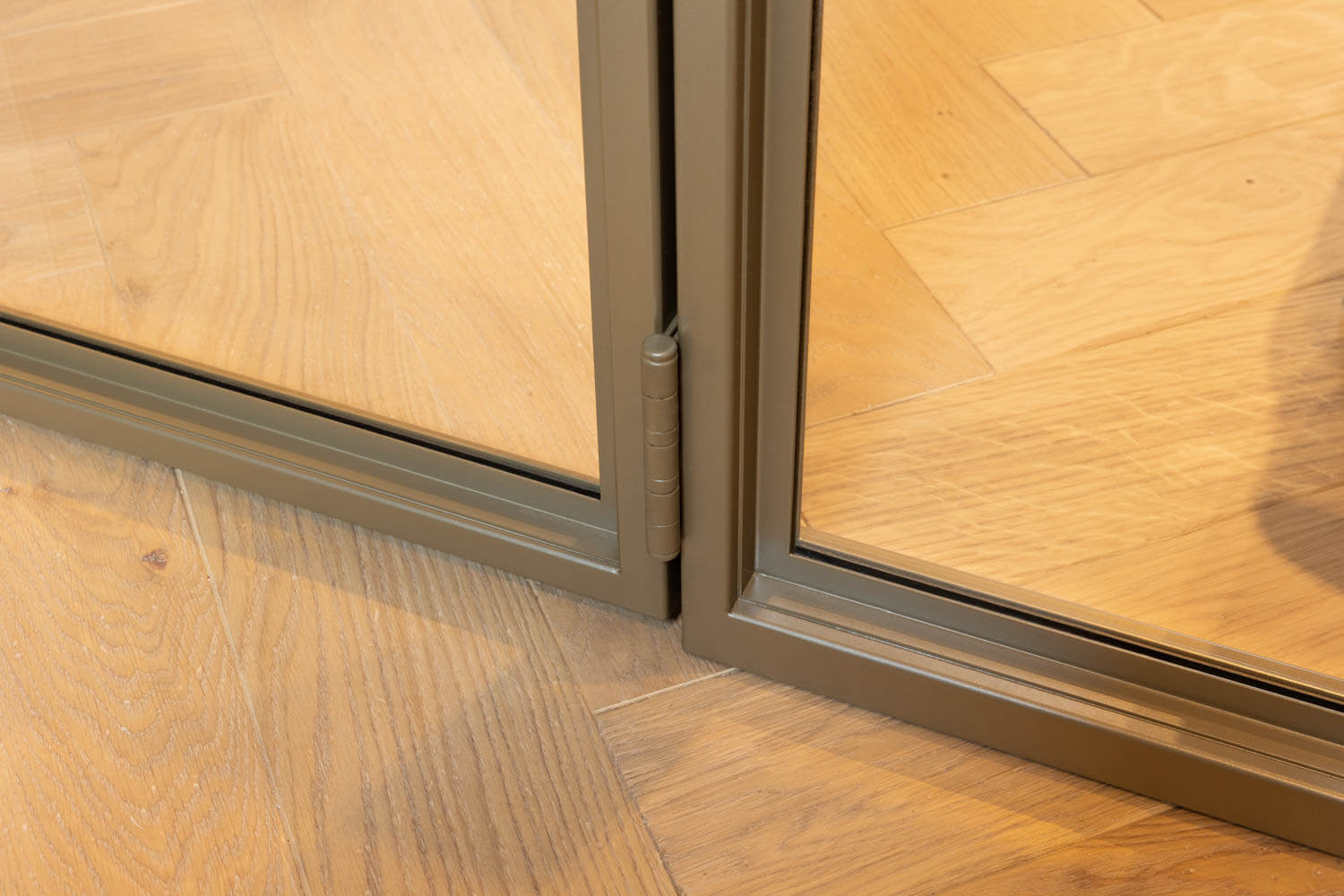 Detail stalen deur met kozijn met een beige coating, geplaatst op een visgraat houten vloer.