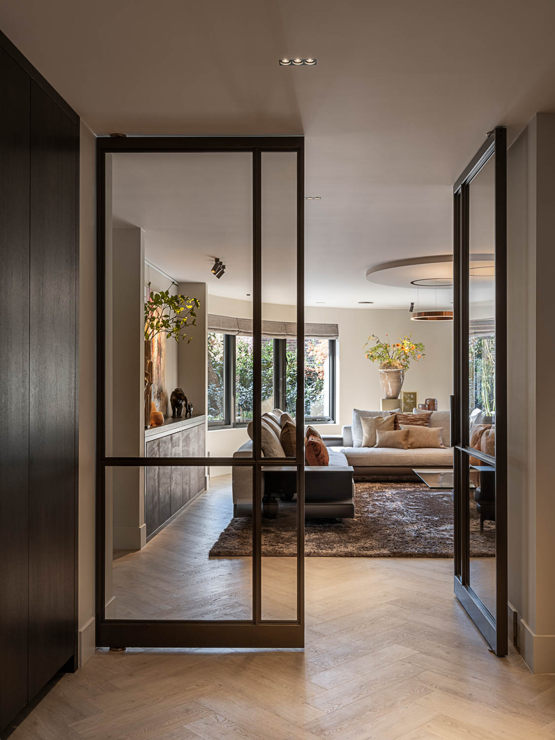 Openstaande bronzen stalen deuren met glas verbinden hal en woonkamer in moderne stijl.