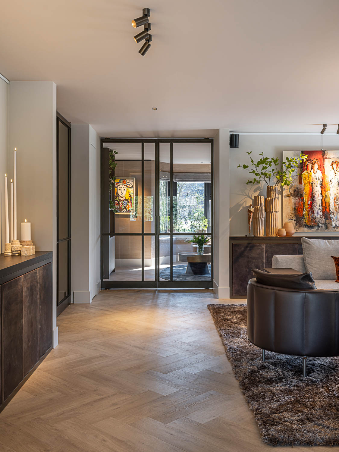 Luxe woonkamer met bronzen stalen deuren, kunst aan de muur en sfeervolle verlichting.