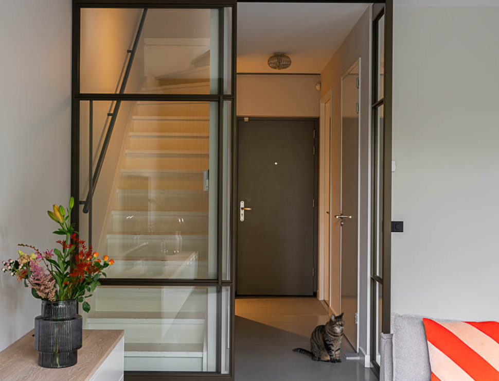 Industriële Anodic Brown stalen roomdivider met glas, scheidend tussen hal en woonkamer, met strakke betonvloer.