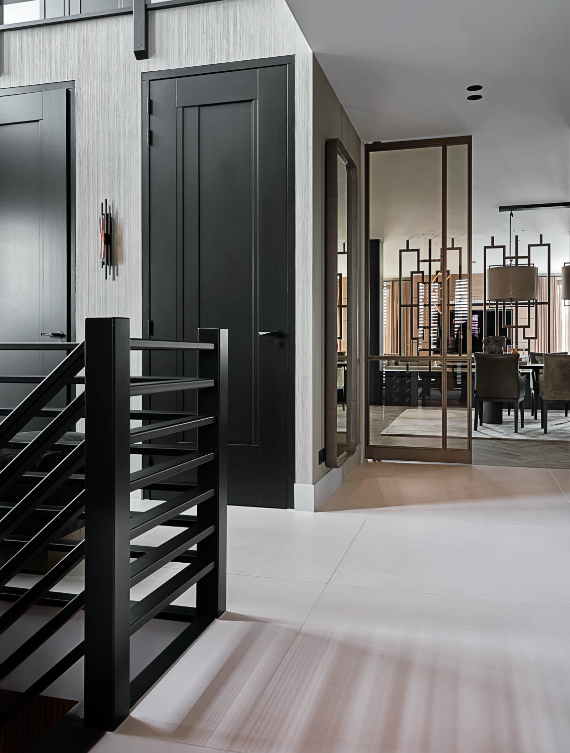 Zwarte stalen trapleuning met zicht op messing stalen binnendeur en luxe eetkamer met geometrisch roomdivider.