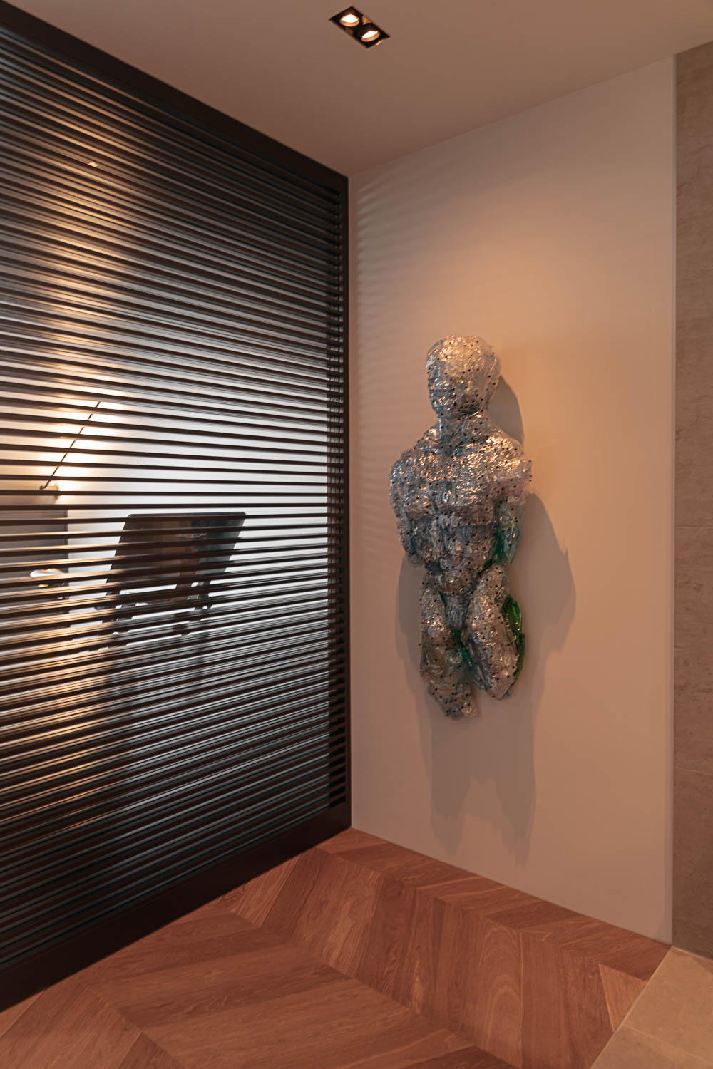 Bronzen stalen schuifdeur met glas in fitnessruimte met kunstobject aan de muur en houten visgraatvloer.
