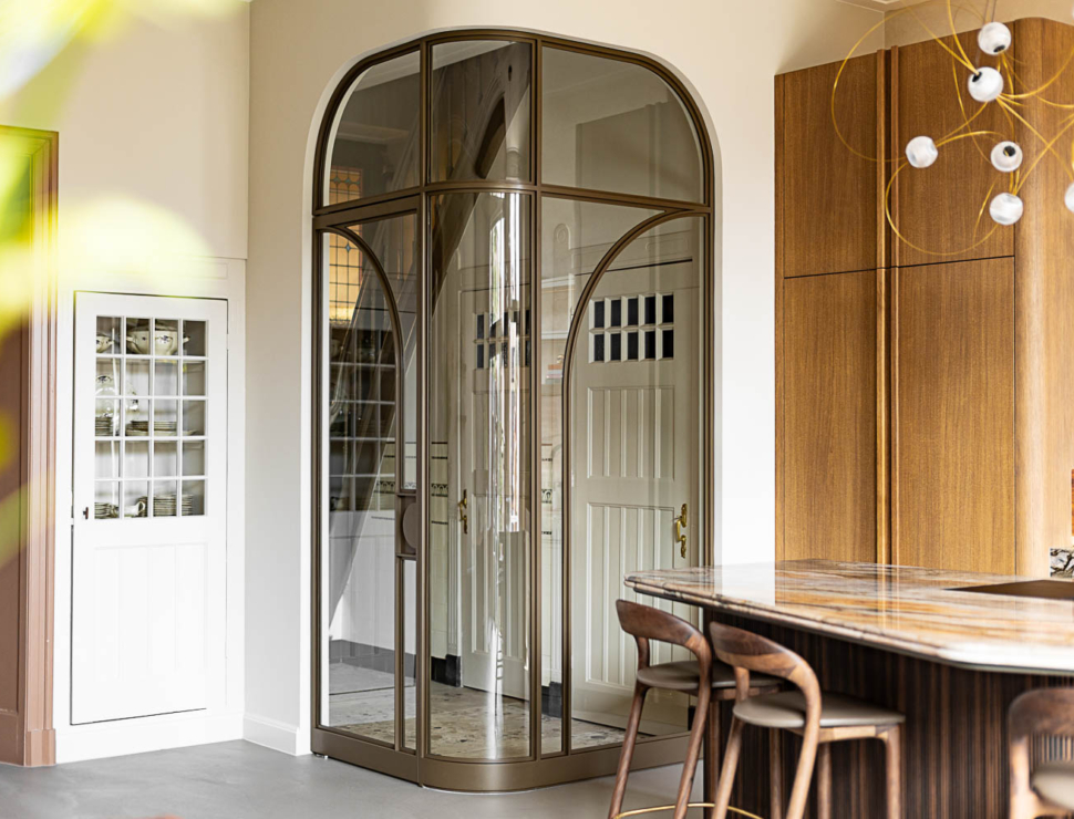 Bronzen stalen roomdivider met rond glaswerk in luxe keuken met hout en marmer.