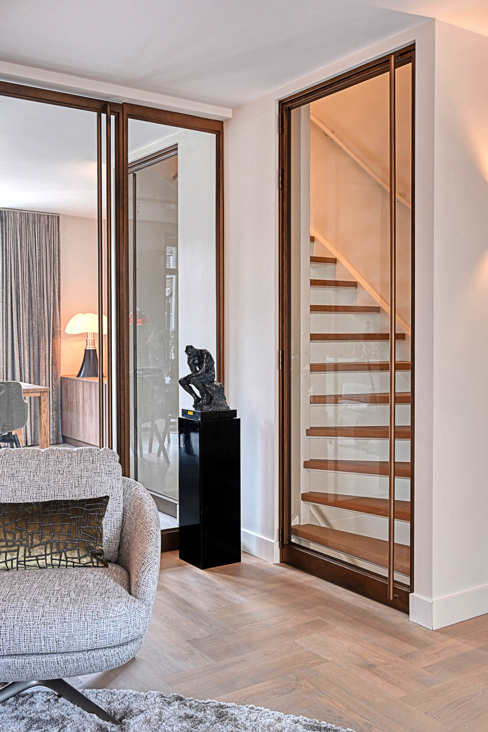 Elegant stalen trapdeur met glas in warme bronscoating, naadloos geïntegreerd in licht en ruimtelijk interieur.