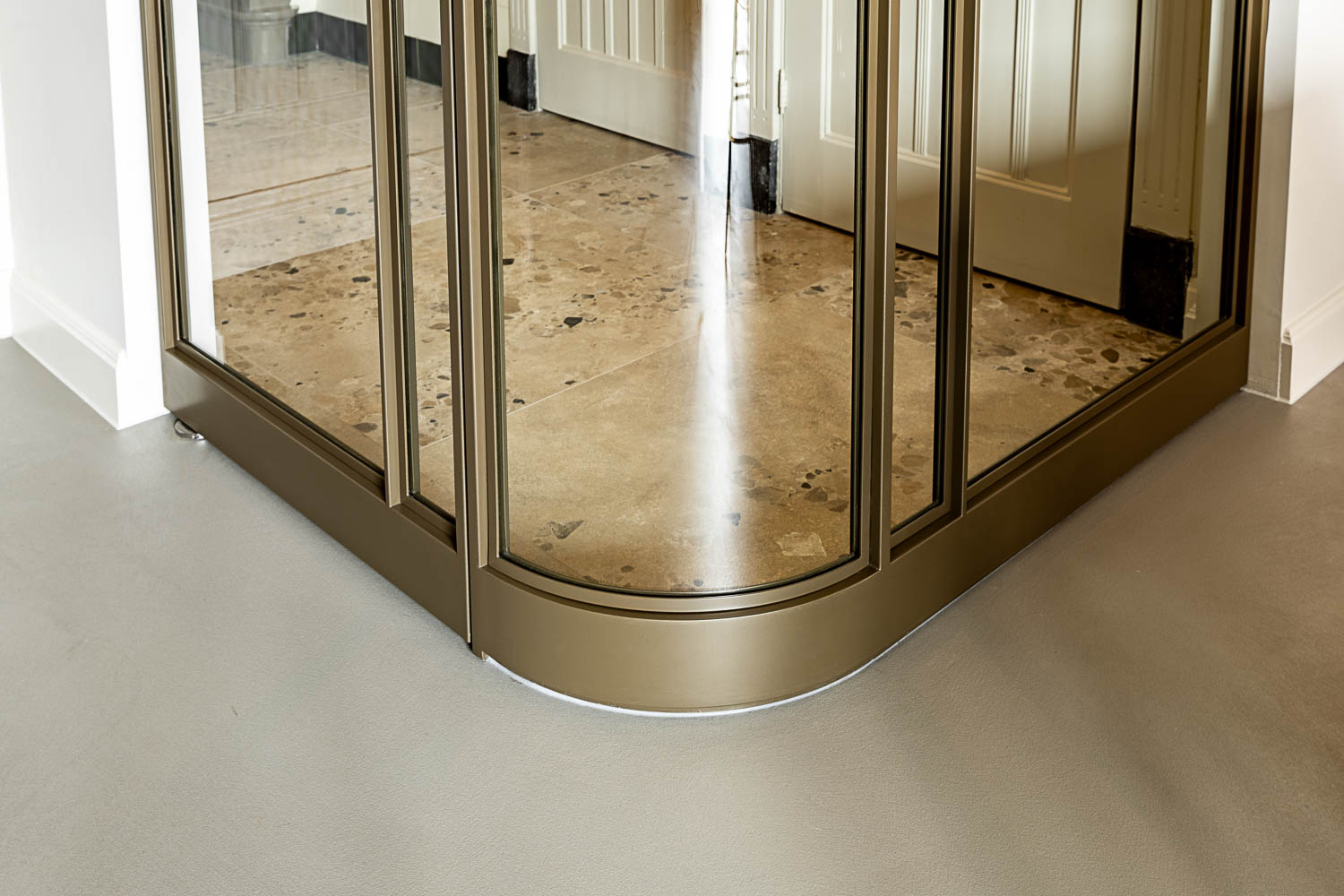 Onderzijde van bronzen stalen glaswand met afgeronde hoek en terrazzo vloer.