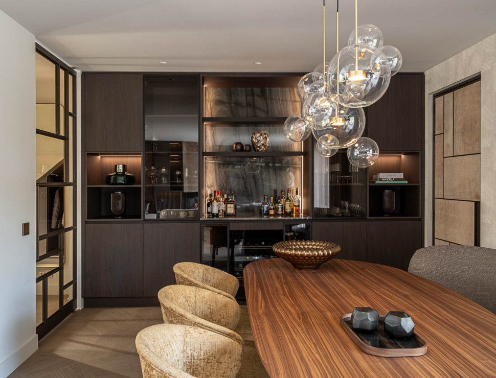 Luxe eetkamer met maatwerk barmeubel in donker hout, glazen stalen deur en opvallende designlamp met glazen bollen.