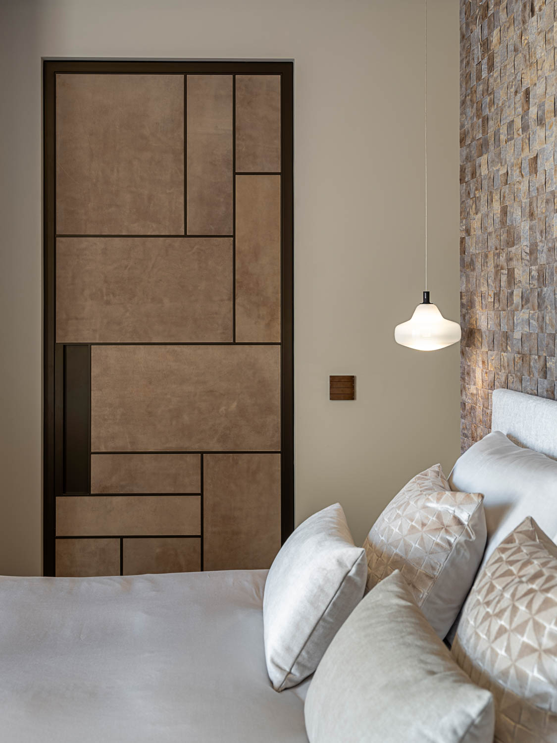 Stijlvolle slaapkamer met een geometrische suède-paneeldeur en luxe gestoffeerd bed met sierkussens.