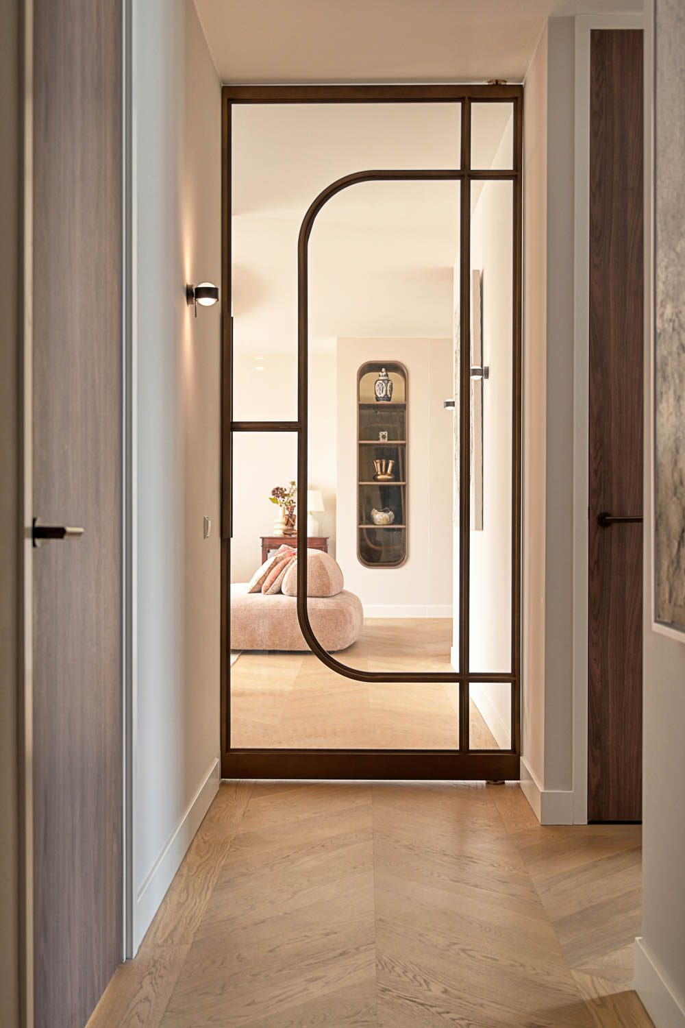 Stalen binnendeur in bronskleur met glas als eyecatcher in luxe hal met visgraatvloer.