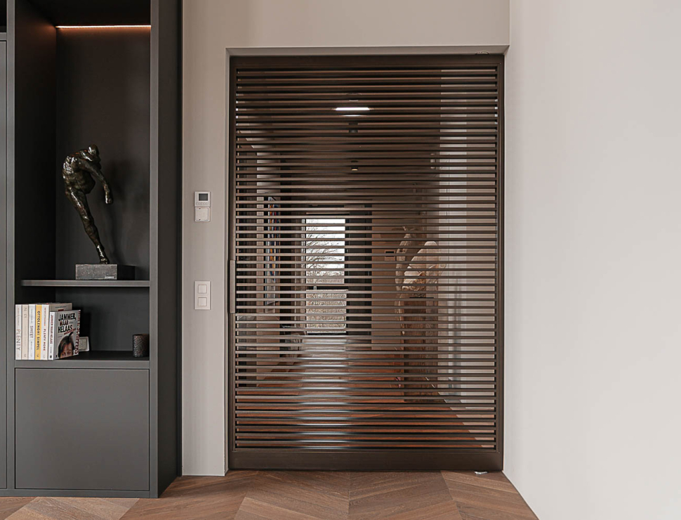 Moderne entree met bronzen stalen taatsdeur, donkere maatwerkkasten en kunstsculptuur in penthouse.