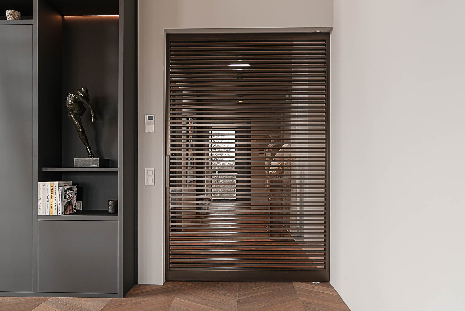 Moderne entree met bronzen stalen taatsdeur, donkere maatwerkkasten en kunstsculptuur in penthouse.