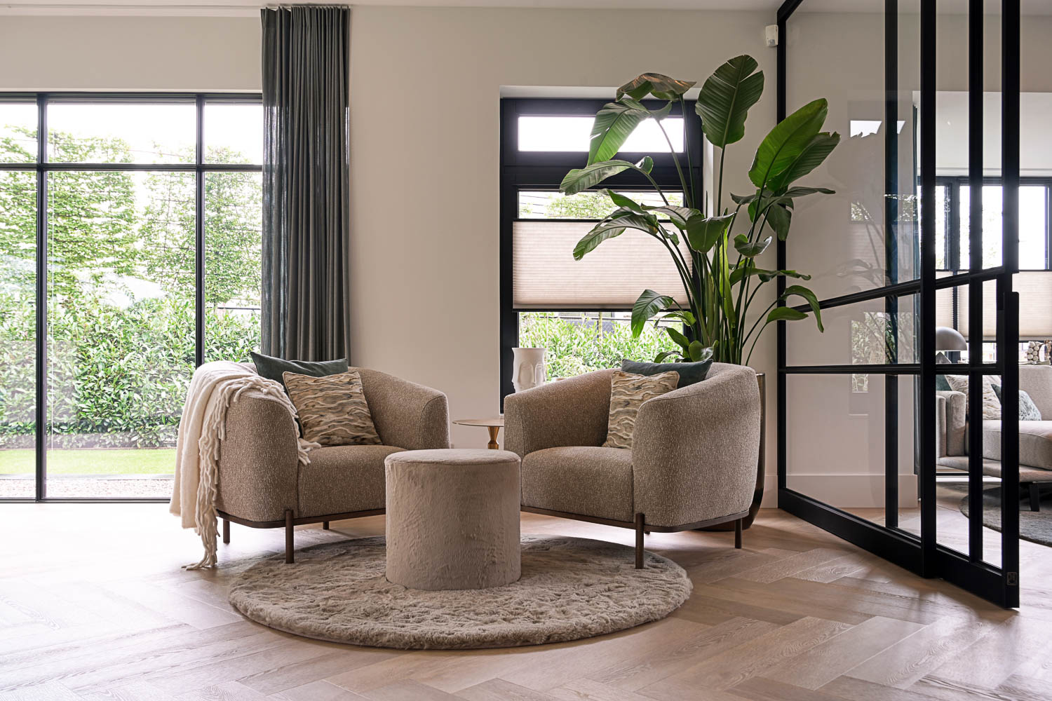 Twee beige designfauteuils in knusse zithoek met zwarte stalen schuifdeuren en grote kamerplant.