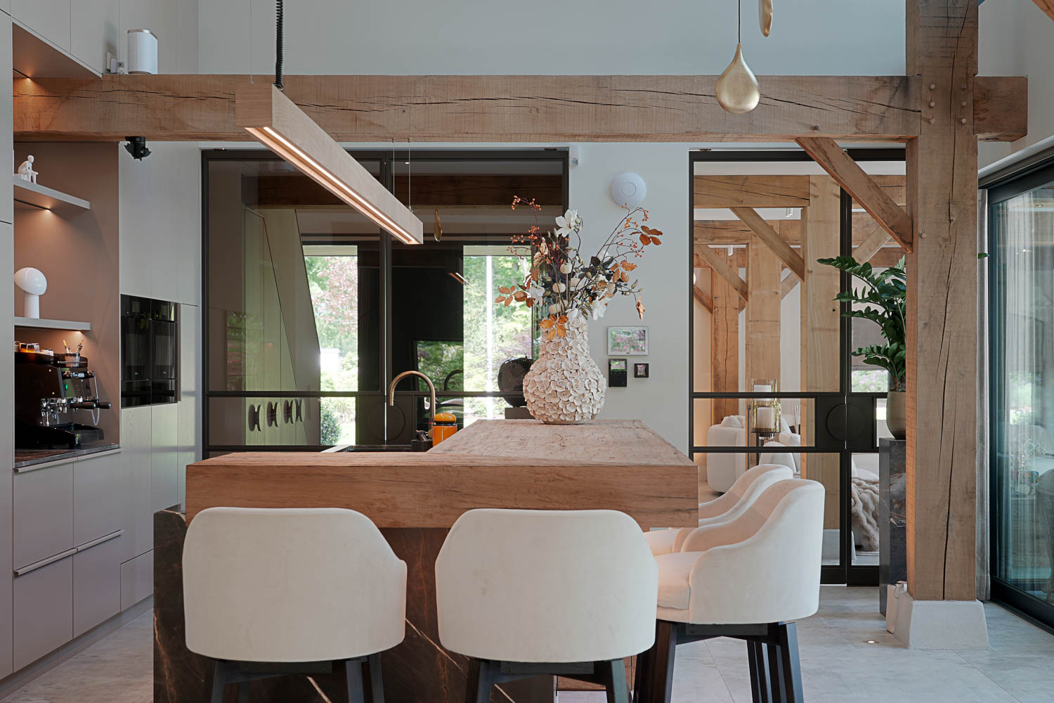 Open woonkeuken met zwarte stalen taatsdeuren, houten balken en luxe kookeiland.