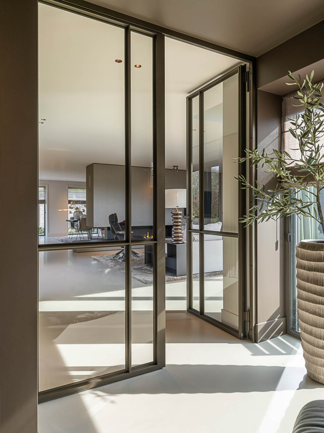 Dubbele stalen scharnierdeuren in Anodic Brown met glas creëren rust en privacy in moderne woonvilla.