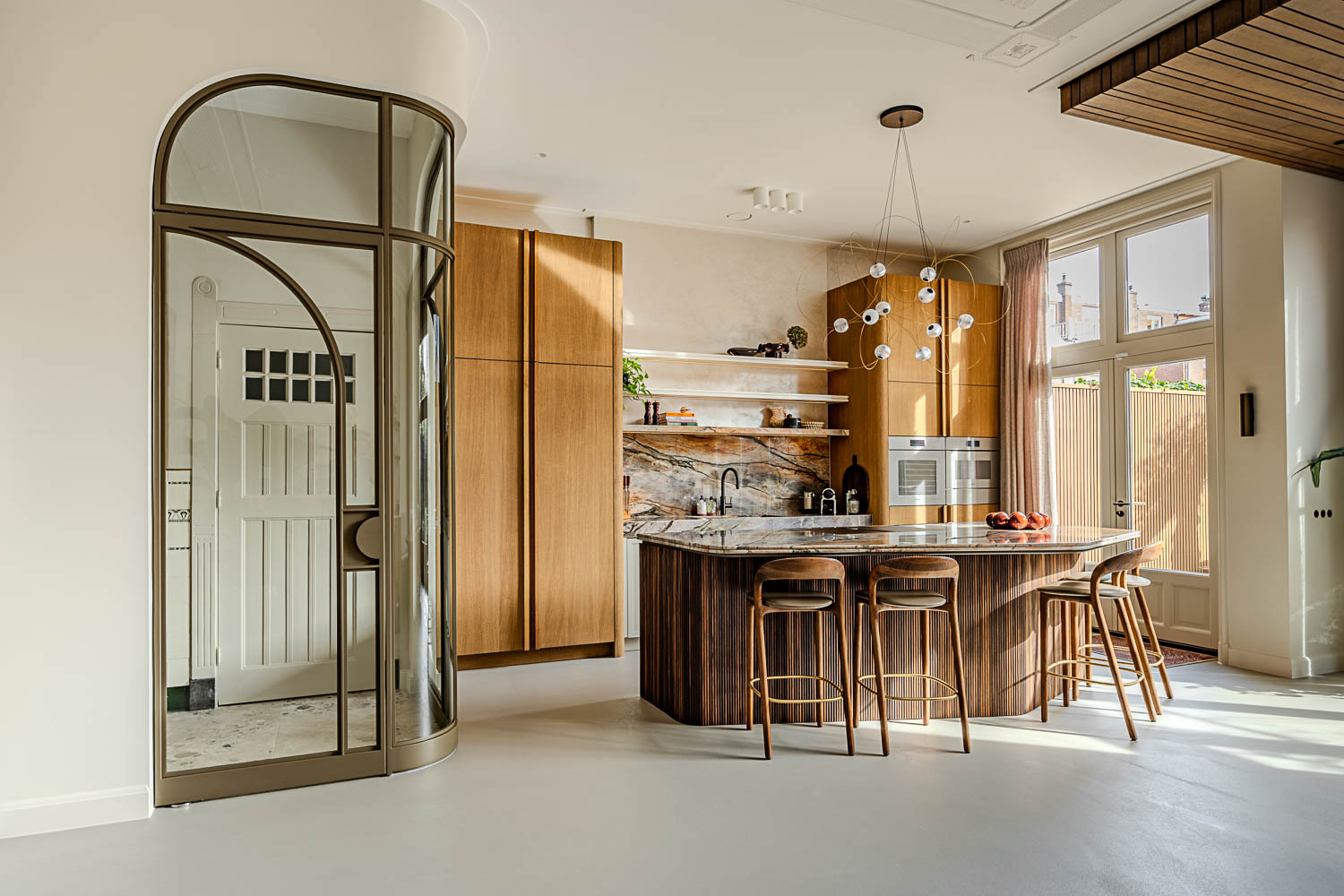 Bronzen ronde stalen glasdeur naast luxe keuken met hout, marmer en designverlichting.