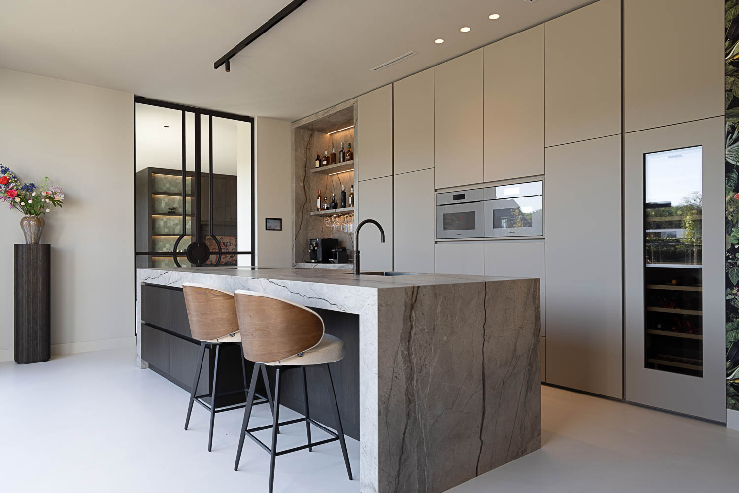 Grijsbruine stalen deuren met glas en ronde details naast een lichte designkeuken met natuurstenen kookeiland.
