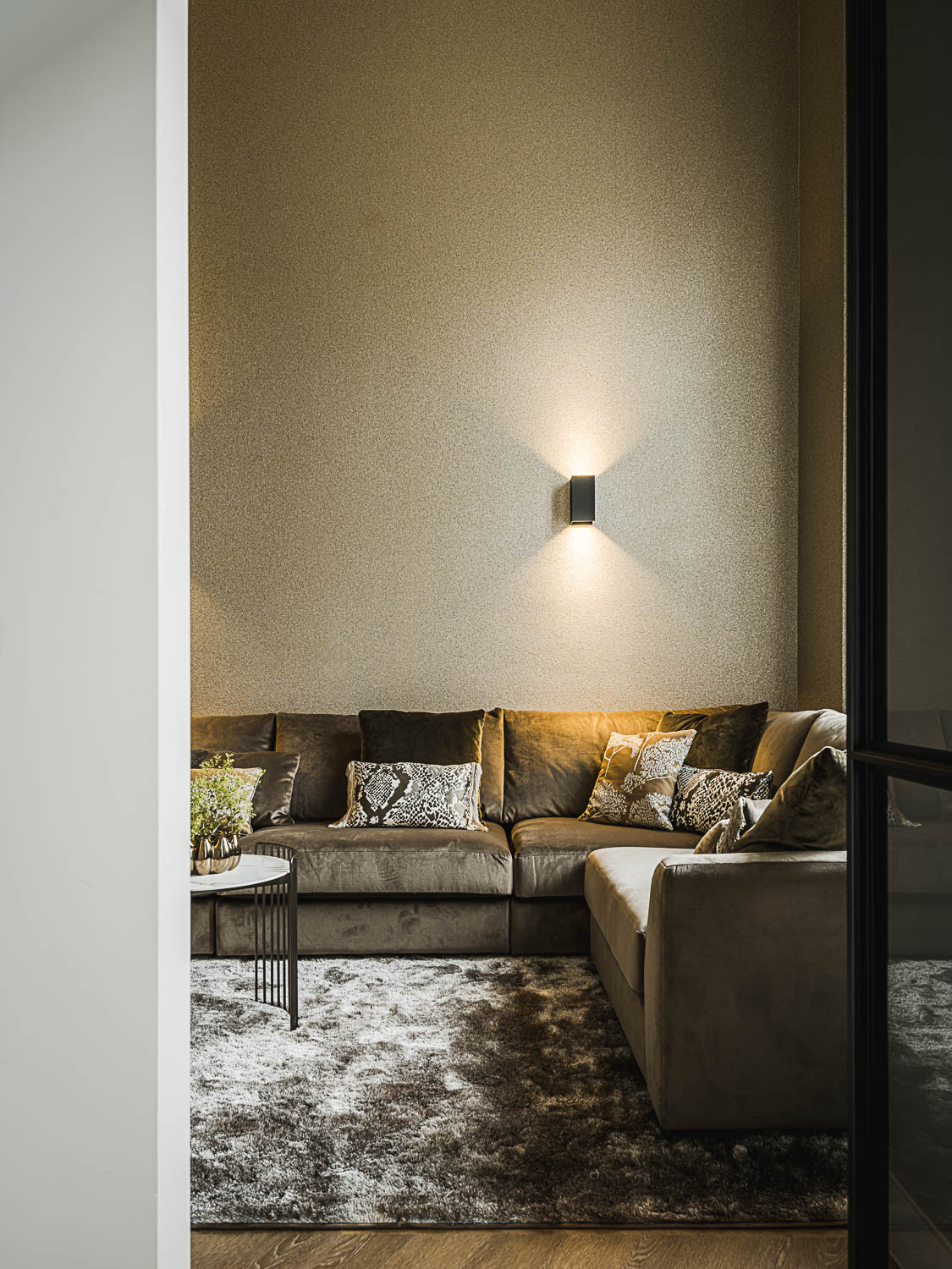Zithoek met fluwelen hoekbank en zwarte stalen deur in modern interieur.